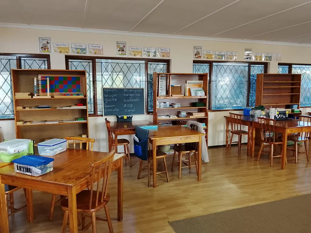 A classroom with wooden desks, bookshelves and a chalkboard, seasons charts above the windows