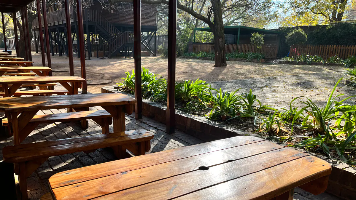 Wooden benches and tables on a covered veranda beside a garden
