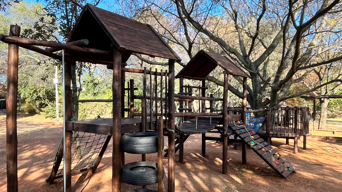 Wooden climbing frames and a slide under mature trees